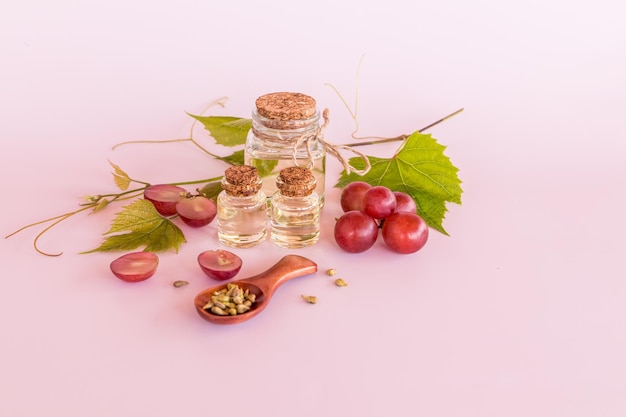 Three different glass bottles with cork cap with natural organic grape seed oil on a pink background and a bunch of grapes natural oils