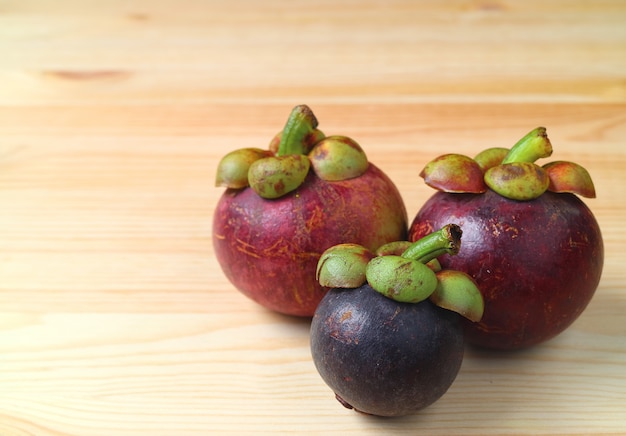 Photo three different size and color ripe purple mangosteen fruits on the wooden table