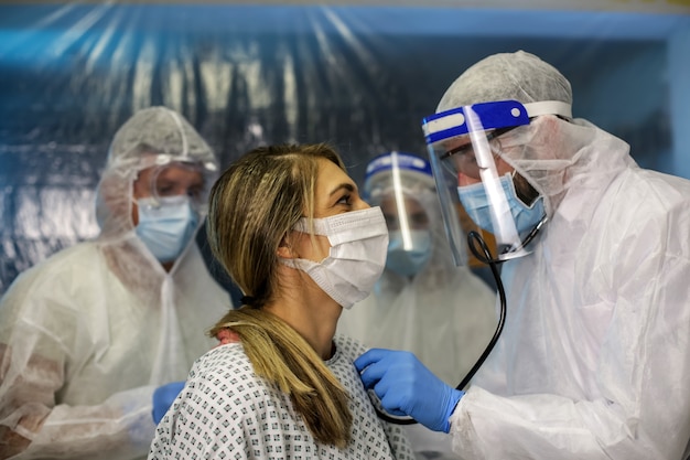 Three doctors in protective suits are examining the patient. Hospital field
