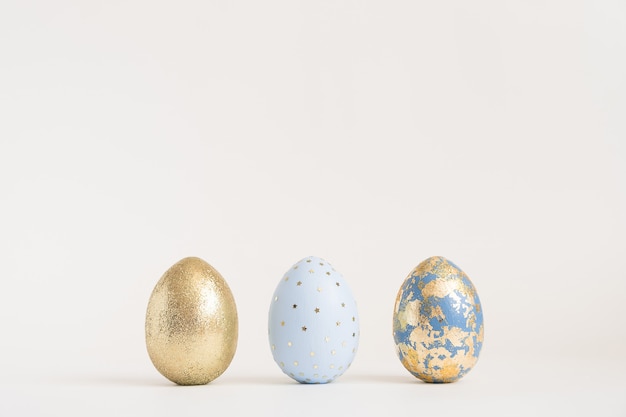 Three Easter golden decorated eggs on blue surface. Minimal easter concept. 