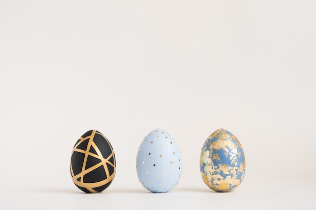 Three Easter golden decorated eggs on blue surface. Minimal easter concept. 