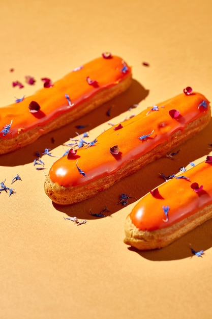 Three eclairs with orange glaze and custard on an orange background Creative layout Creative food poster