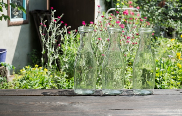 Three empty glass bottles on a dark board on a garden background