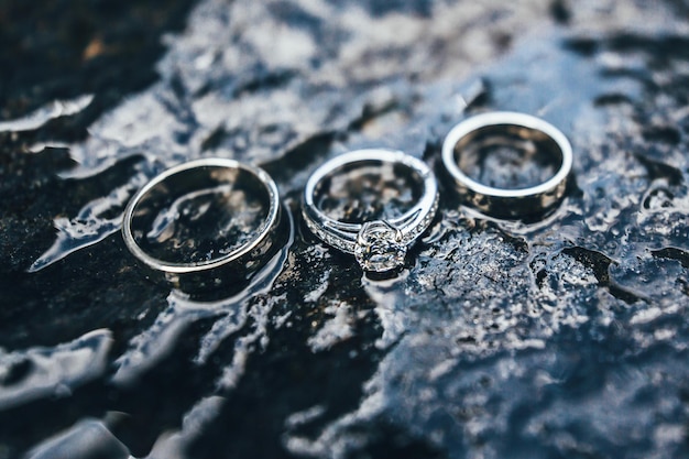 Photo three engagement rings with diamonds photographed on wet stone nature background abstract background