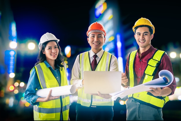 Three engineer male and female with blueprint and computer on bright Modern night Japan city with Furturistic light.