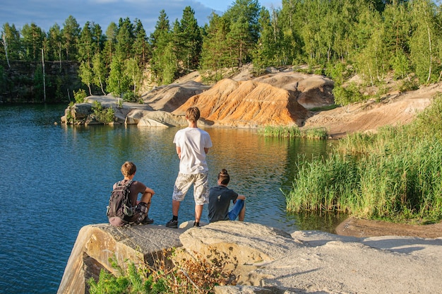 Three friends sit on a rock above a deep and beautiful granite quarry