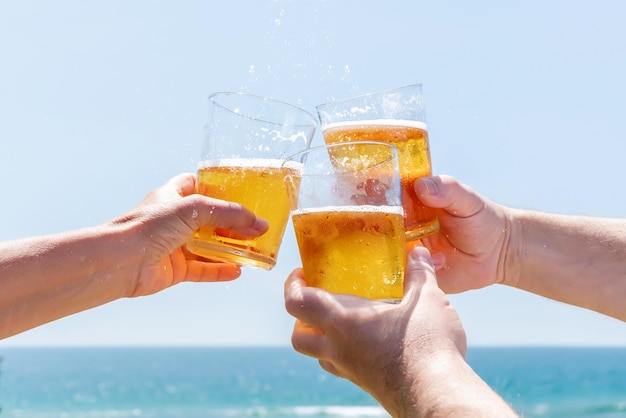 Three friends toasting with beer on a beach in front of the sea Happy and fun summer