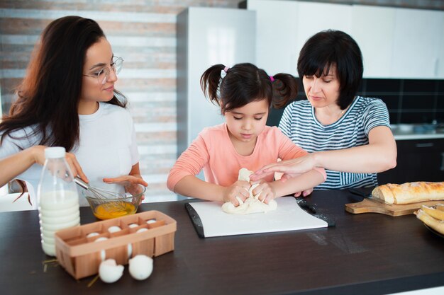 Three generations of women cook in the kitchen. Grandmother, mother teach granddaughter to cook. They knead the dough together.