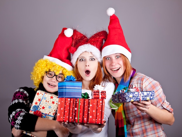 Three girlfriends in funny hats with christmas gifts. Studio shot.