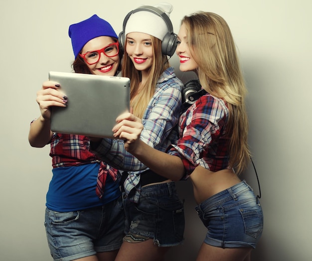 Three girls friends taking selfie with digital tablet studio shot over gray background