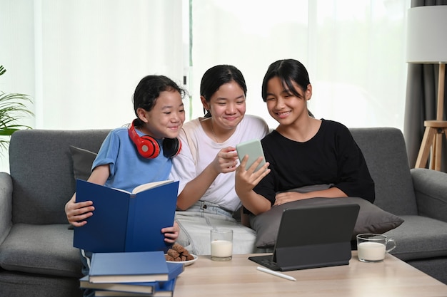 Three girls watching something funny on smart phone while siting together on couch in living room.