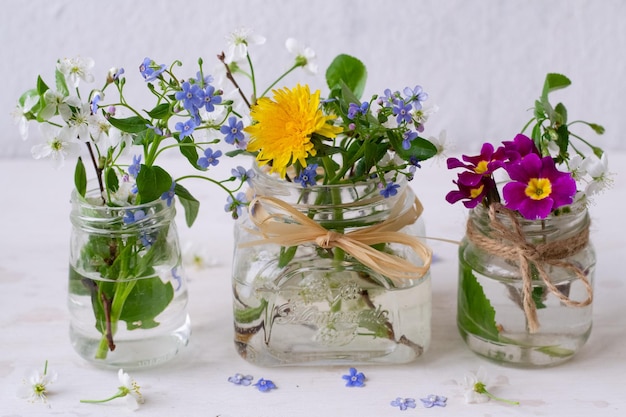 Three glass jars of flowers with a ribbon tied around them one of which says'dandelions '