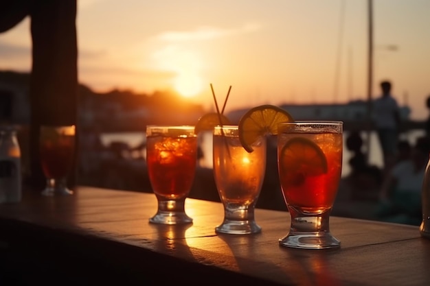 Photo three glasses of cocktails sit on a ledge with the sun setting behind them.