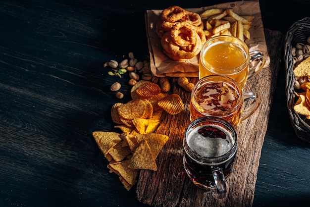 Three glasses of expensive craft beer, classic and unfiltered and dark in a glass on the table with a snack of peanut and pistachio chips and nachos