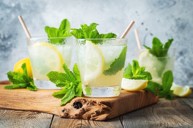 Three glasses of mojito cocktail on wooden cutting board