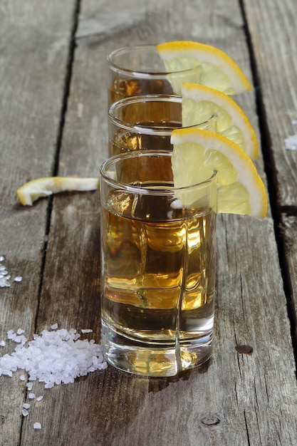 Three glasses of tequila with lemon and salt on a wooden table