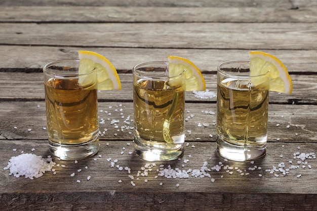 Three glasses of tequila with lemon and salt on a wooden table