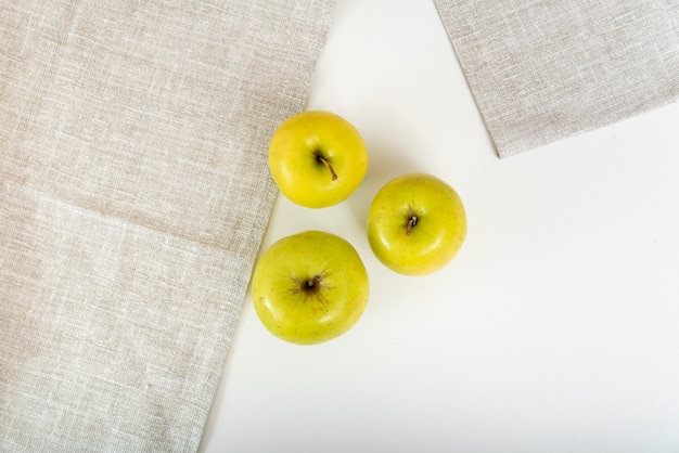 Three green apples are on table next to textile napkins. Top view.