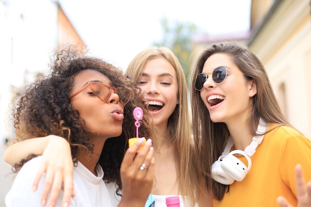 Three happy beautiful women blowing soap bubbles in city street.