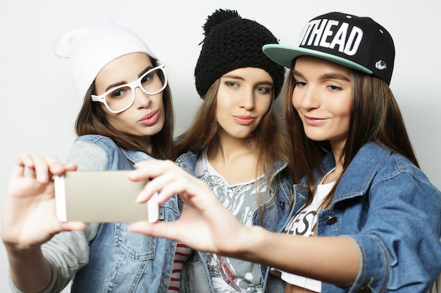 Three happy teenage hipster  girls with smartphone taking selfie