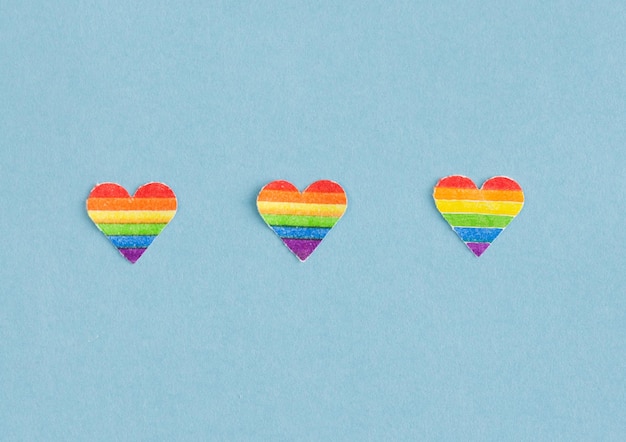 Three hearts with LGBTQ colors in a row on a blue background Copy space