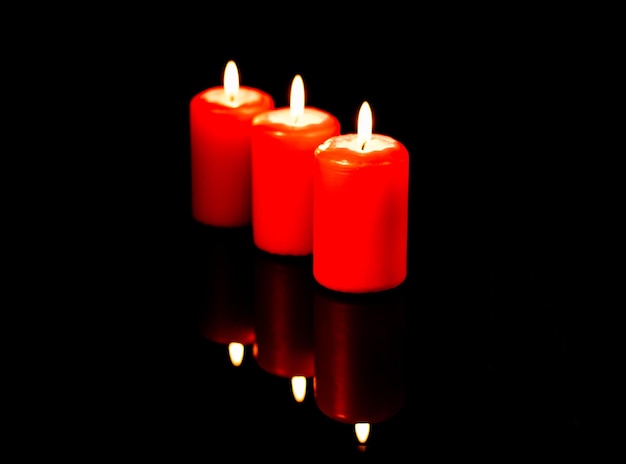 Three hot red candles arranged diagonally are reflected against the background of a black mirror