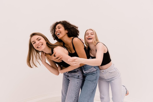 Three interracial young women wearing top and jeans in good mood spend time together on white background