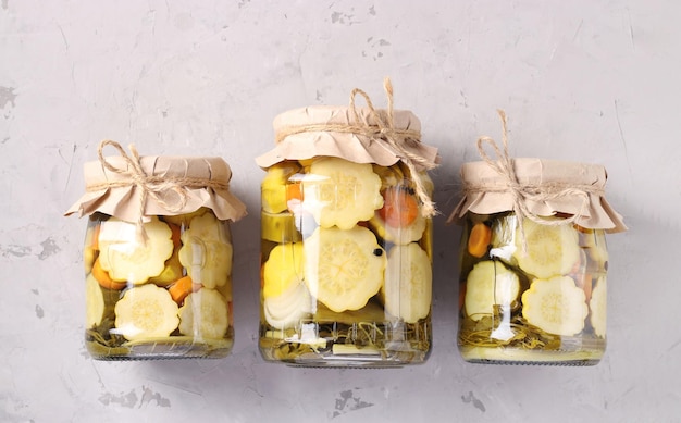 Three jars of pickled patissons with cucumbers on light gray background Top view Horizontal format