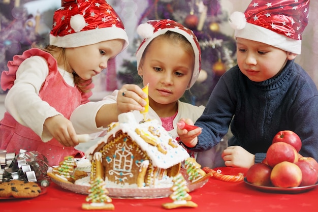 Three kids in caps decorated gingerbread house