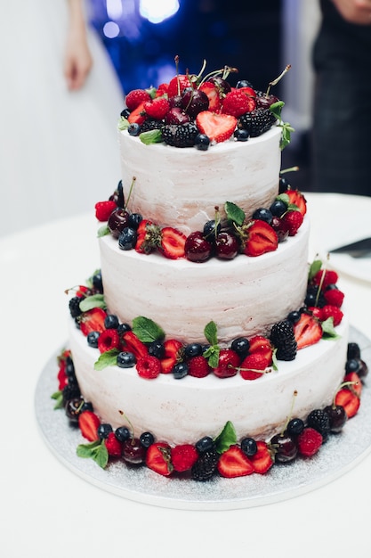 Three-layered wedding cake with fresh berries.Decorated with strawberry, blueberry, cherry and blackberry.