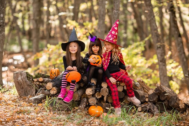 Three little girls in halloween witch costumes laugh conjure walk through the autumn forest