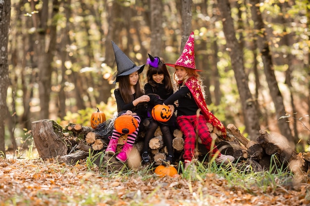 Three little girls in halloween witch costumes laugh conjure walk through the autumn forest