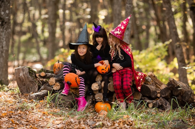 Three little girls in halloween witch costumes laugh conjure walk through the autumn forest