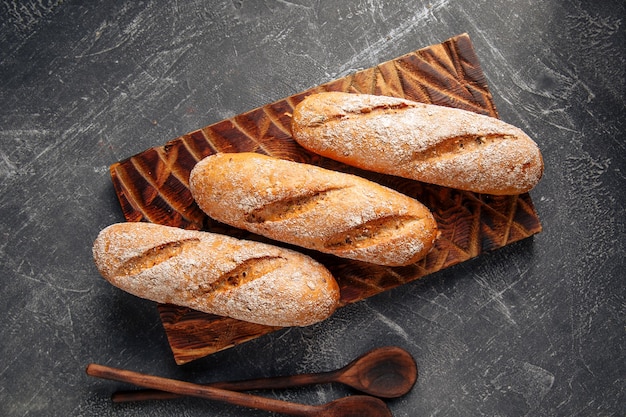 Three loafs of fresh baked baguette on the wooden cutting board on gray background