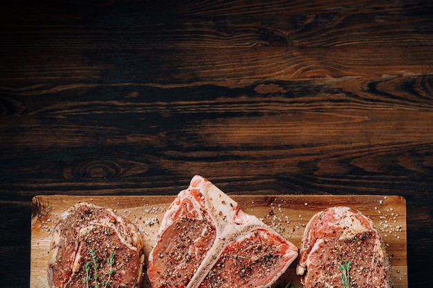 Three lovely raw marbled black Angus beef steaks flavored with a mixture of ground pepper and ready to cook and serve on a dark wooden background