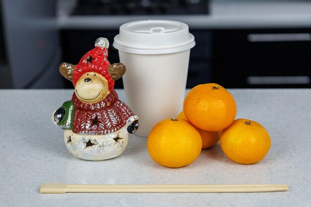 Three Mandarins and chopsticks a Christmas figurine and candies on a white table against a dark kitchen background