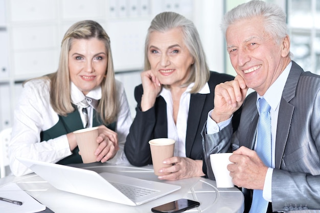 Three mature businesspeople using laptop and drinking coffee