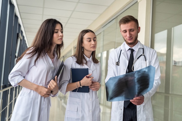 Three medical intern looking through x-ray image of lungs for viral pneumonia of Covid-19 patient in clinic. Medical concept