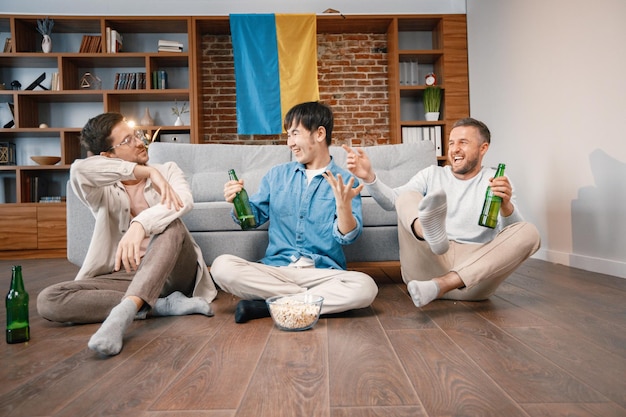 Three men watching a football game on tv and drinking a beer