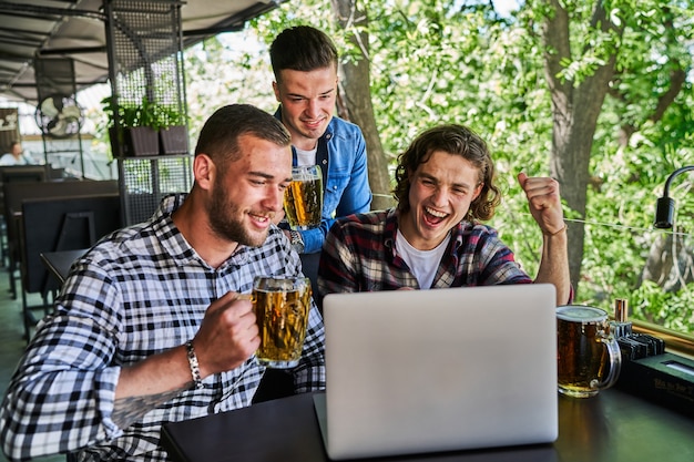 Three men watching football in a pub and drinking beer.