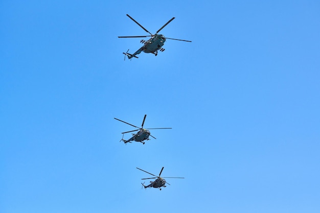 Three military helicopters flying in bright blue sky while performing demonstration flight, copy space. Aerobatic team performs flight at air show