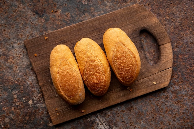 Three mini French baguettes in wooden cutting board on old reddish brown rust metal texture background top view flat lay vintage food theme design concept