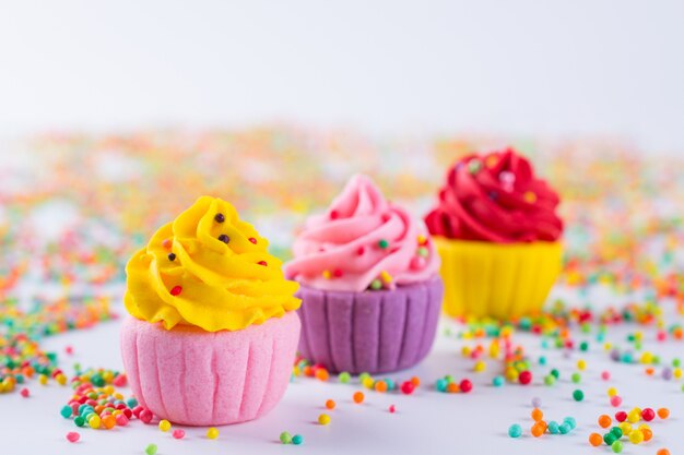 Three miniature multicolored sugar  cupcakes on light background with sprinkles