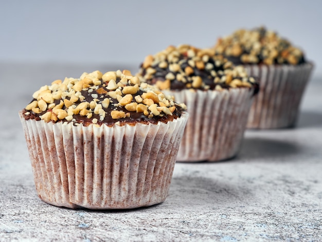 Three muffins with peanuts and chocolate glaze in line