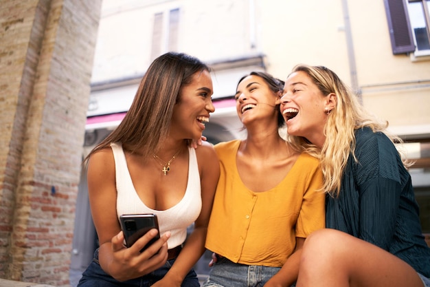 Three multiracial women using mobile phone outdoors youth and social media networking