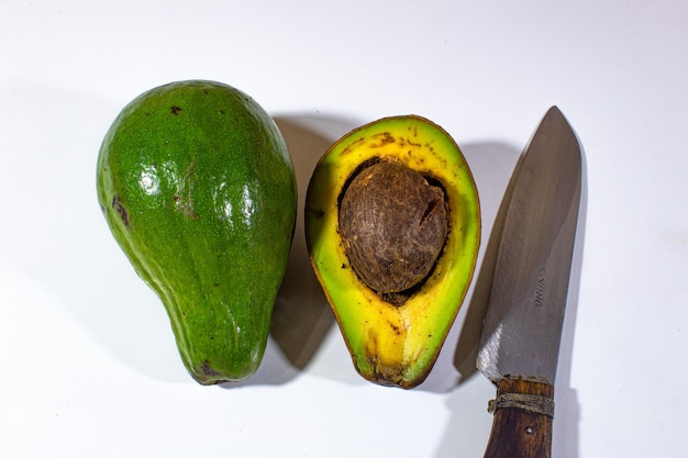 three objects a green avocado which has been cut and a knife are presented on a plain white backg