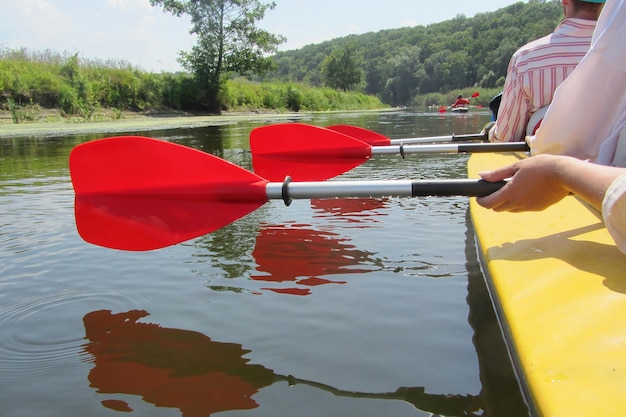 Three paddles are displayed in a row in the hands of the people floating in the kayak The paddles are reflected in the calm water the floating people in the yellow kayak are holding red paddles