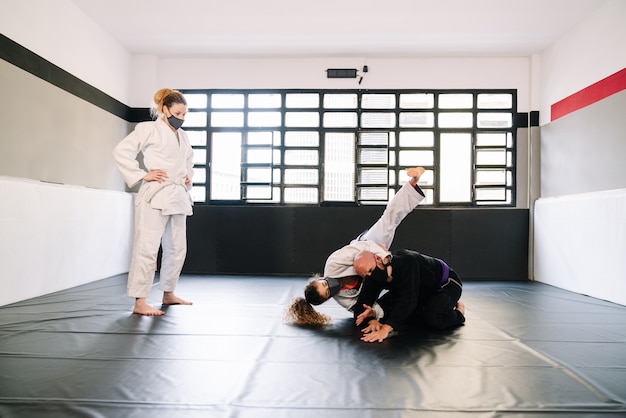 Three partners in a martial arts training practicing techniques on the gym mat all wearing face masks due to the covid 19