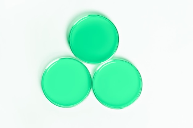 Three Petri dishes with green liquid On a white light background View from above