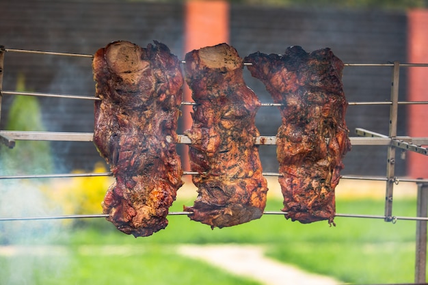 Three pieces of pork shish kebab are seasoned with spices and cooked on a skewer above the fire near the house in warm weather